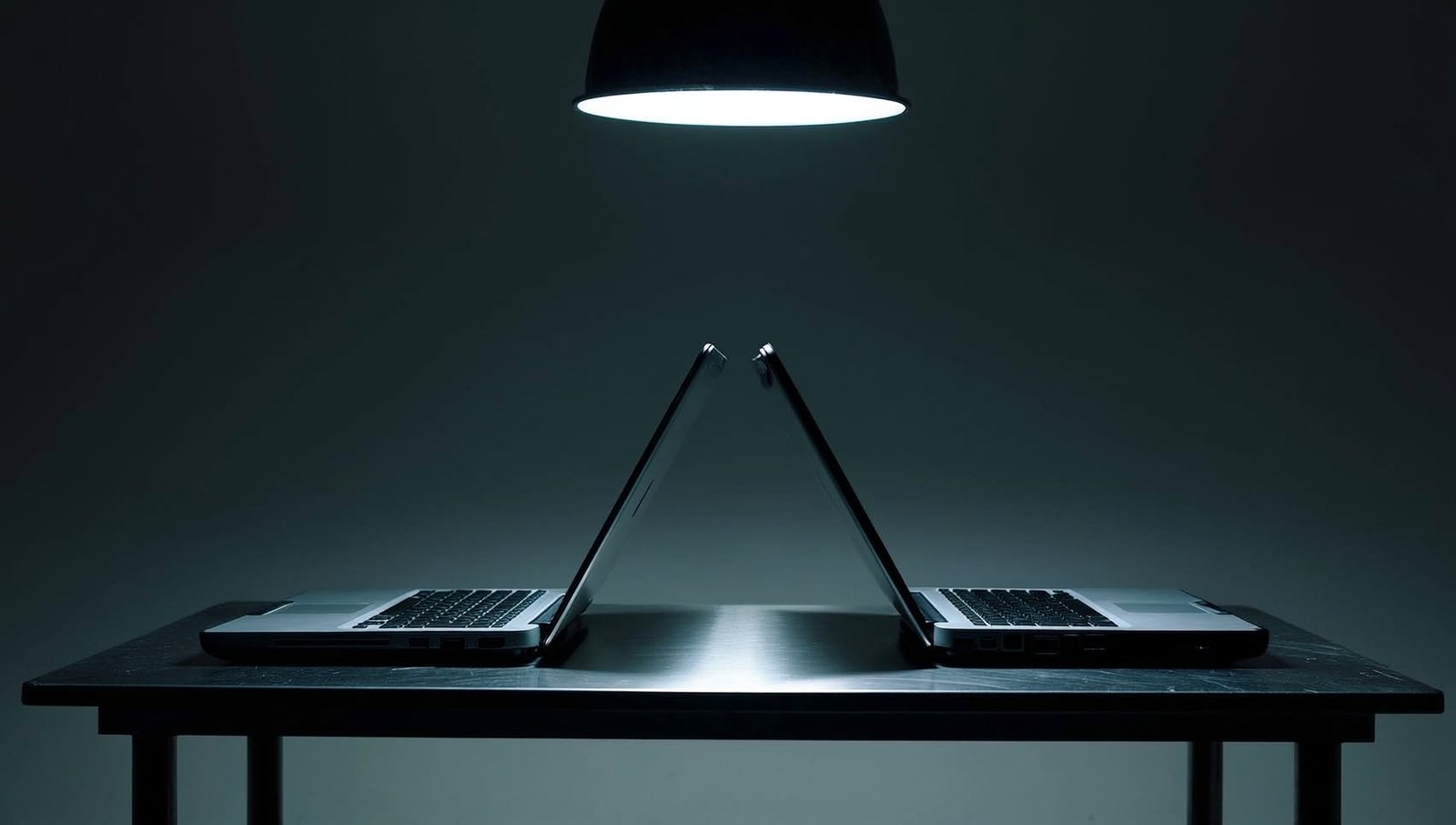 Two mechanical keyboards facing each other on a workbench under a single hanging lamp.